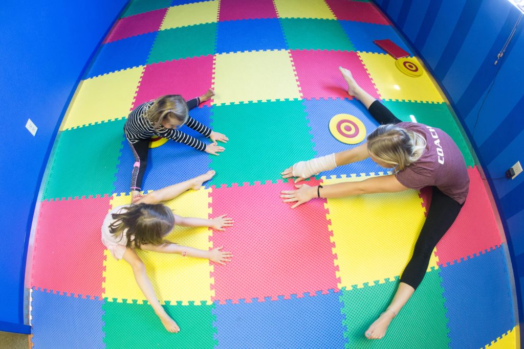 Coach stretching with young toddlers on colorful mats at High Altitude Tumbling in Provo